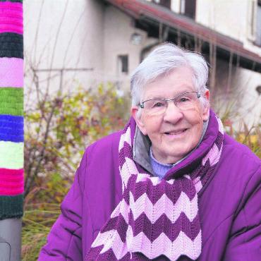 Vor ihr ist Wolle nie sicher - Auch den Schal hat sie selber gestrickt. Lotti Koller neben einem von ihr umstrickten Leuchtkandelaber. Bild: Annemarie Keusch