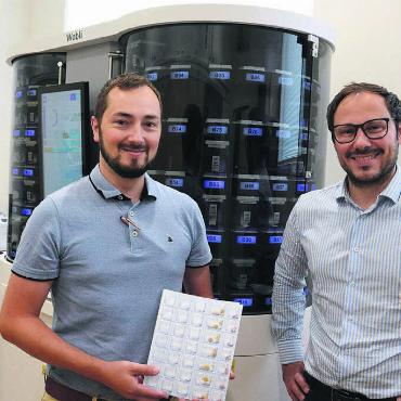 Mehr Zeit für die Kunden haben - Alain (links) und Pascal Jost mit ihrem neusten «Mitarbeiter», dem Dossierroboter VBM 200F, genannt Wobli. Er übernimmt in Zukunft das Bestücken der Wochenblister, wie ihn Alain Jost in der Hand hält. Bild: Chregi Hansen