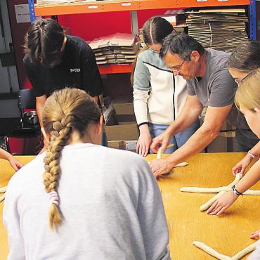 Backen neben der Baustelle - Unter fachkundiger Anleitung von Pit Waltenspül fällt das Zopfflechten den Schülern nicht mehr schwer. Bild: mo