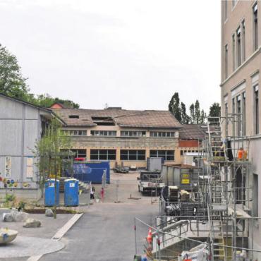 Härtetest für Schulraumstrategie - Baustelle Schulort, eine Aufnahme, die Wohlens Gesamtsituation rund um den Schulraum zeigt: Das alte Primarschulhaus (rechts) ist saniert und erstrahlt ab sofort in neuem Glanz, während die Bauarbeiten an der Bezirksschule (Mitte) begonnen haben. Links das veraltete «Providurium», das noch zwei Jahre halten muss. Bild: Daniel Marti