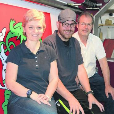 Erfolgsgeschichte fortführen - Sie sind bereits ein eingespieltes Team und arbeiten Hand in Hand: Firmengründer und jetziger Inhaber Samuel Keller und seine Nachfolger, Adrian und Monika von Arx (von rechts) vor dem Herzstück des Betriebs, dem grossen Textildrucker. Hier wird gerade eine Fahne der ehemaligen Bündner Gemeinde Schlans ausgedruckt. Bild: Chregi Hansen
