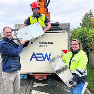Fast komplett auf LED - Gemeinderat Christoph Meyer (links) reicht Monteur Yannic Walter symbolisch eine der letzten LED-Leuchten, während Projektleiterin Sonja Hengartner die ausgemusterte Natriumdampflampe hält. Bild: zg