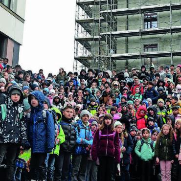 Wie eine Art Brückenbauer - Grosse Freude: Die Schulkinder posierten samt Lehrkräften vor den beiden Schulhäusern, dem neuen Primarschulhaus und dem sanierten Altbau (rechts). Bild: Daniel Marti