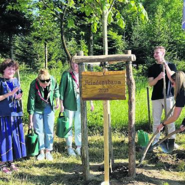 Vom Nussbaum zur Sommerlinde - Symbolischer Spatenstich für den Friedensbaum 2025 durch eine Gruppe von Jungwacht und Blauring, mit Applaus verdankt von (v. l.): Herbie Wiederkehr, Gemeindeammann Arsène Perroud und Künstlerin Heidi Widmer. Bild: Walter Minder