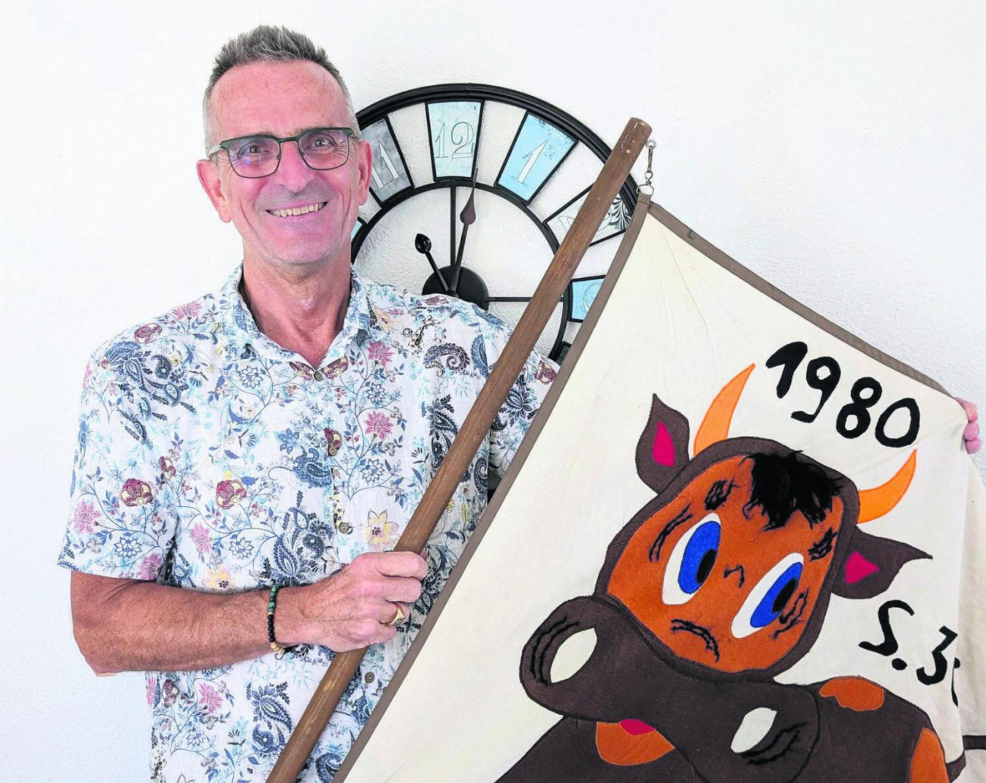 Guido Wirth mit der 1980 selbst gebastelten Fahne seines allerersten Klassenlagers als Lehrer. Im Hintergrund die Uhr, die er nach der Räumung seines Büros bewusst als Letztes abhängen will. Bild: Marco Huwyler