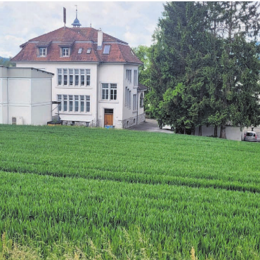 Fokus auf Kindergarten - Hier, hinter dem Schulhaus und neben dem Provisorium, soll schon bald ein Doppelkindergarten stehen. Das Land befindet sich im Besitz der Gemeinde. Am Montag geht es um einen Projektierungskredit. Bild: Chregi Hansen